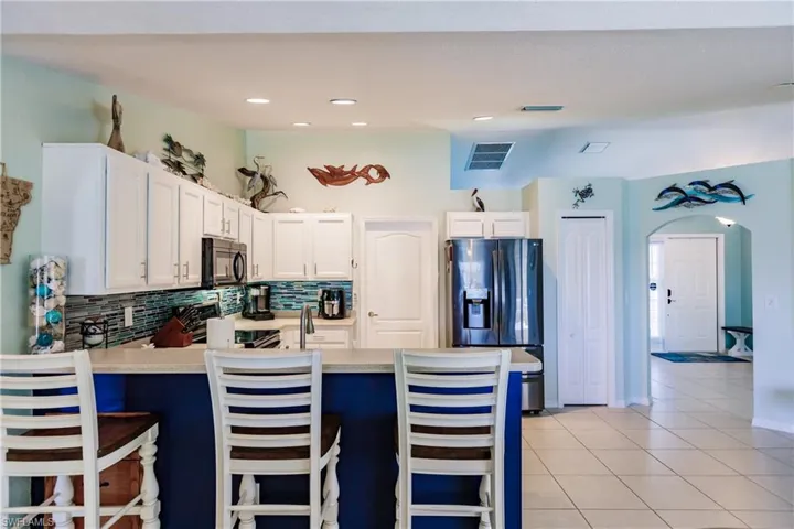 Kitchen featuring kitchen peninsula, stainless steel appliances, backsplash, white cabinets, and light tile floors