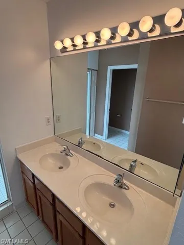 Double vanity with integrated sinks, wood-finish cabinetry, and a full-width mirror with overhead globe lighting