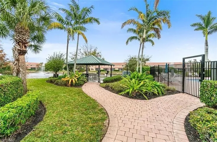 Outdoor amenities featuring a paved pathway, lush landscaping, mature palm trees, a covered gazebo, and a fenced pool area