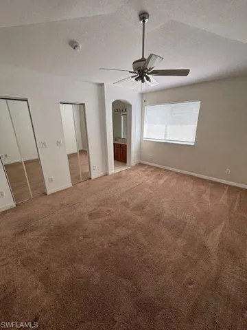 Spacious room featuring ceiling fan, brown carpeting, a window with blinds, and dual mirrored closet doors