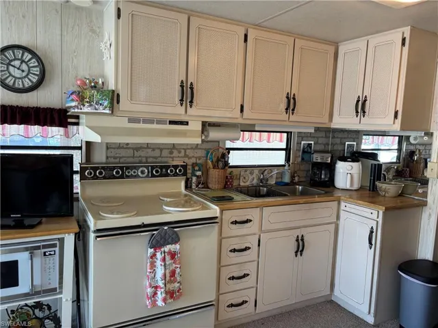 Kitchen featuring white appliances, under cabinet range hood, light countertops, and healthy amount of natural light