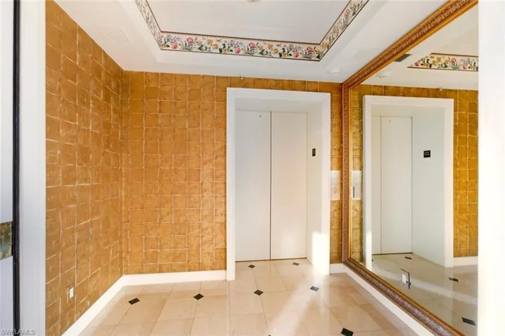 Tiled empty room with a tray ceiling, elevator, and tile walls