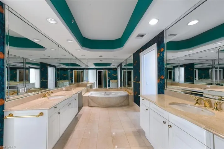 Bathroom featuring a garden tub, a tray ceiling, recessed lighting, two vanities, and light tile patterned floors