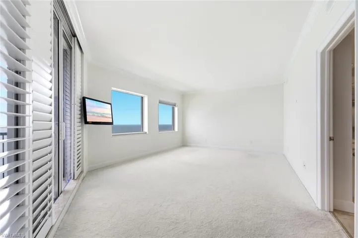 Spacious room featuring large format square tile flooring, a tray ceiling with recessed lighting, and a full-wall glass sliding door system opening to a balcony with a metal railing