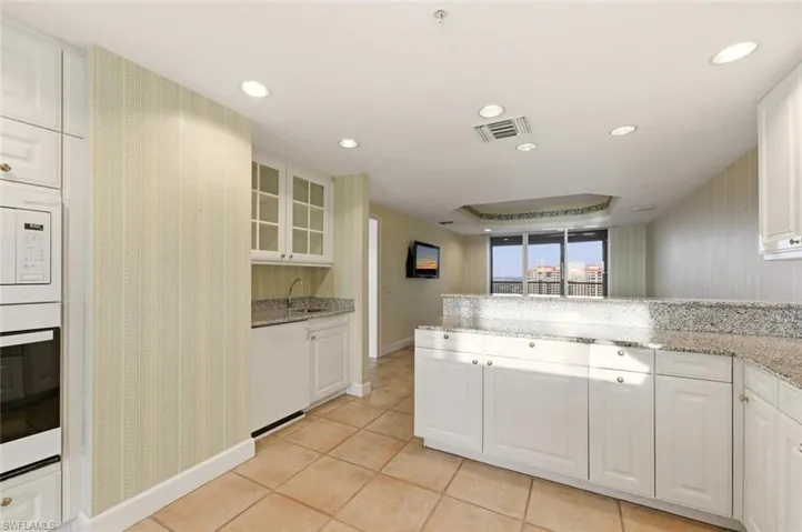 Kitchen featuring white cabinets, light stone countertops, white appliances, light tile patterned floors, and glass insert cabinets