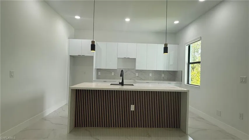 Modern kitchen featuring a waterfall island with slatted wood-finish paneling, white shaker cabinetry, an integrated sink with a matte black faucet, recessed lighting, and pendant lighting fixtures