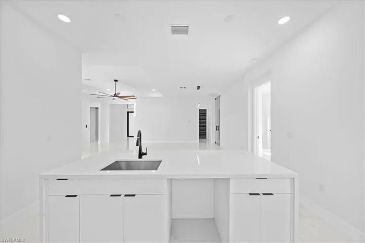 Kitchen island featuring a single-basin sink with a matte black high-arc faucet, white cabinetry with black hardware, and a light-colored countertop