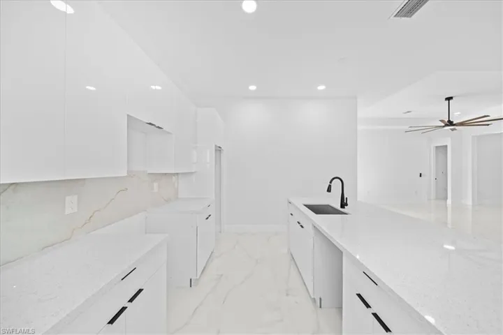 Contemporary kitchen featuring white flat-panel cabinetry, a large center island with a black undermount sink and matte black faucet, recessed lighting, and a marble-patterned backsplash