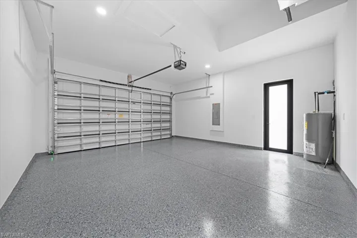 Spacious garage featuring an epoxy floor finish, automatic overhead door, recessed lighting, and a frosted glass-paneled entry door
