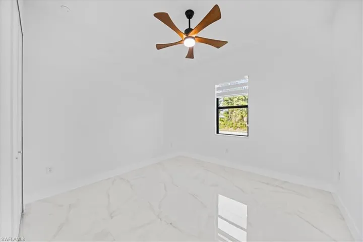 Bright room featuring white walls, a single window with blinds, and white marble-look tile flooring