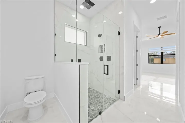 Spacious bathroom featuring a glass-enclosed shower with hexagonal tile flooring and white marble-look wall tiling