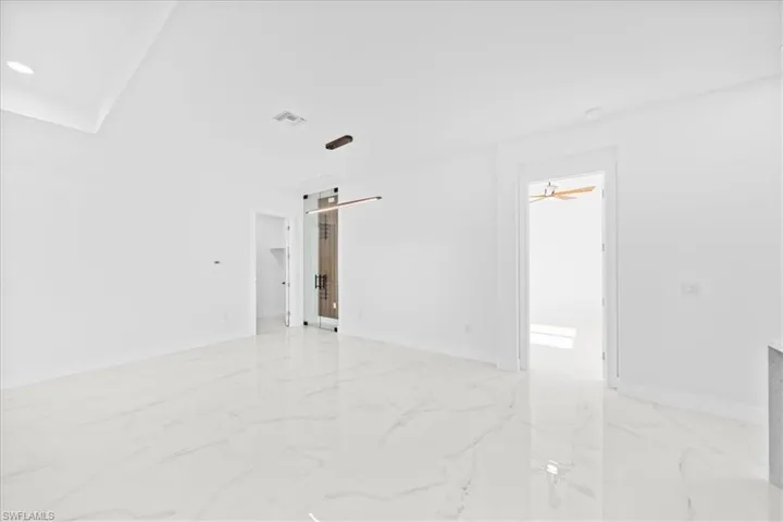 Spacious room featuring white tile flooring with gray veining, a contemporary linear pendant light fixture, a tray ceiling, and recessed lighting