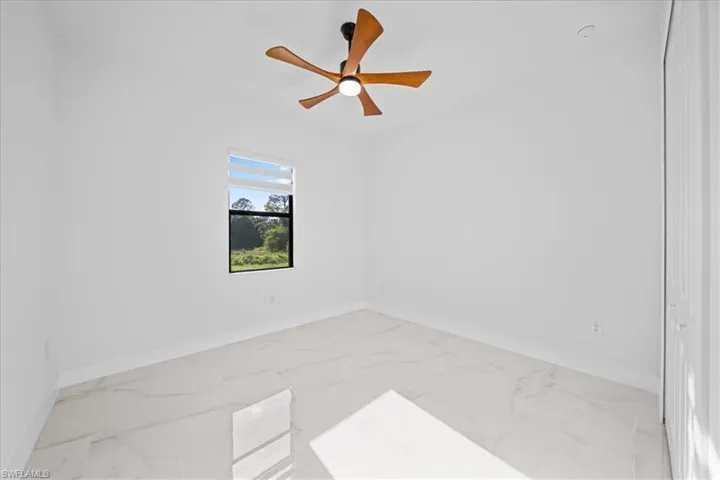 Bright interior space featuring large format tile flooring, a contemporary ceiling fan with wood-finish blades, and a window with natural light