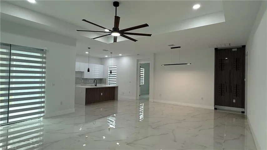 Spacious living area featuring polished marble-look flooring, a large ceiling fan with integrated lighting, and a contemporary linear chandelier