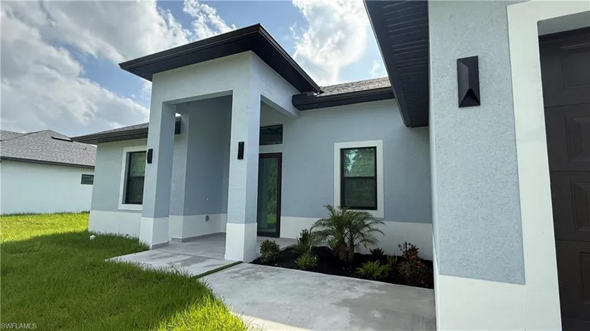 Modern exterior featuring a prominent covered entry, light blue stucco finish, dark trim windows, and complementary landscaping with established plants