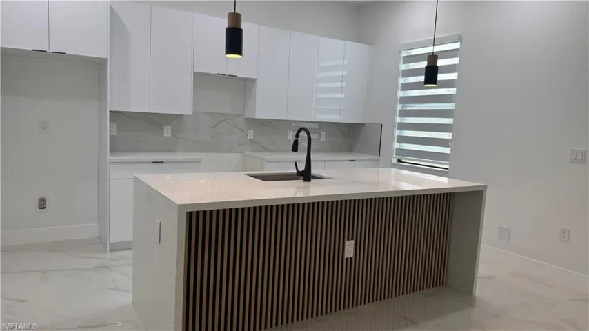 Modern kitchen featuring a waterfall island with slatted wood-finish paneling, an integrated sink with a matte black faucet, and white quartz countertops