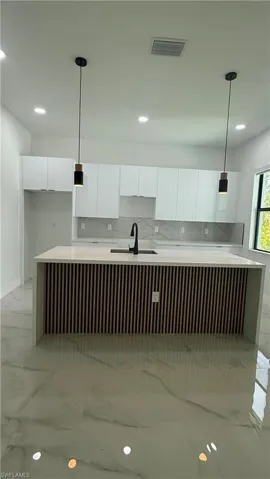Modern kitchen featuring a central island with slatted wood-finish paneling, white quartz countertops, and a matte black single-handle faucet