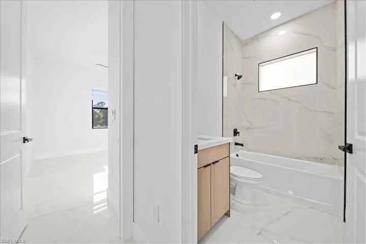 Bathroom featuring a light wood-finish vanity with a stone-finish countertop, a white bathtub, and full-height tile surround