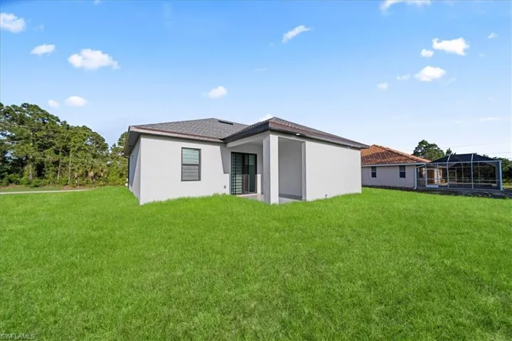 Spacious backyard with manicured lawn, featuring a covered patio and a sliding glass door entry