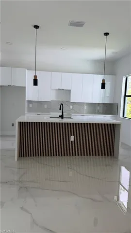Contemporary kitchen featuring a large center island with slatted wood-finish paneling, white stone-finish countertops, and matching full-height backsplash