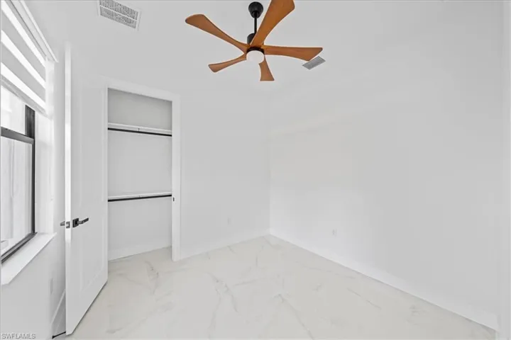 Bright room featuring a modern ceiling fan, white walls, and large format white tile flooring with veining