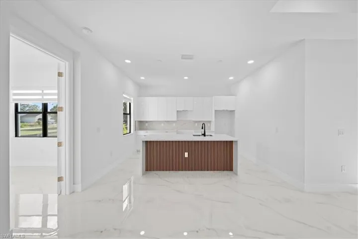 Open-concept kitchen featuring an island with slatted wood-finish detailing, white cabinetry, a black faucet, and recessed lighting