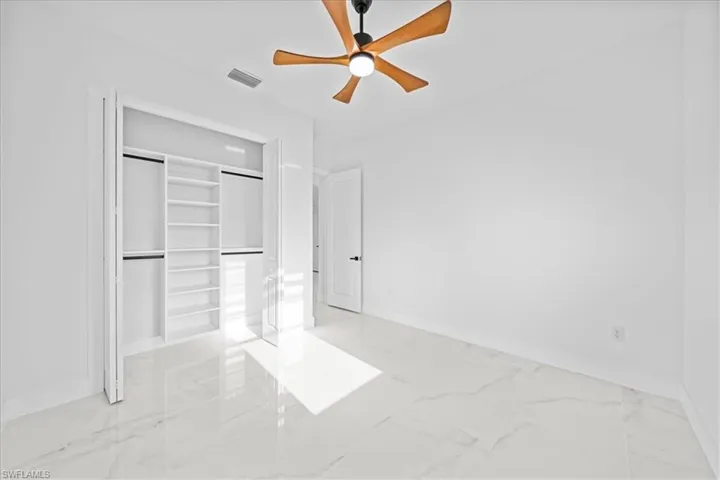 Bright interior space featuring large format marble-look tile flooring, a ceiling fan with wooden blades, and a built-in closet organization system with shelving and hanging rods