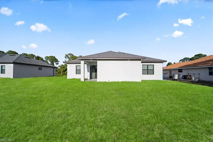 Expansive green lawn with a contemporary single-story home featuring a covered patio, dark framed windows, and a dark shingle roof