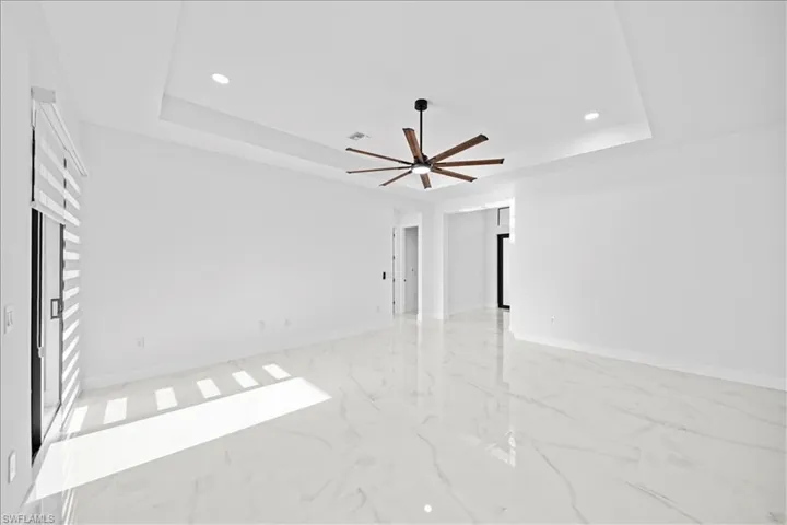 Spacious interior featuring a tray ceiling with recessed lighting, large format tile flooring, a contemporary ceiling fan with wood-finish blades, and a sliding glass door with horizontal blinds