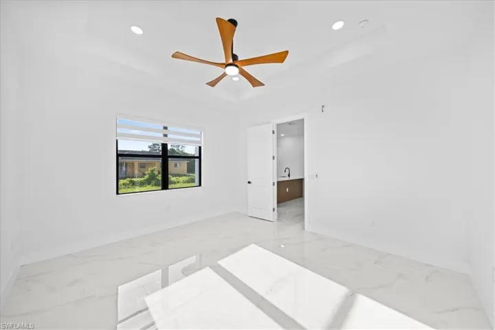 Recessed ceiling with an integrated ceiling fan, large window with layered blinds, white tile flooring, and white walls