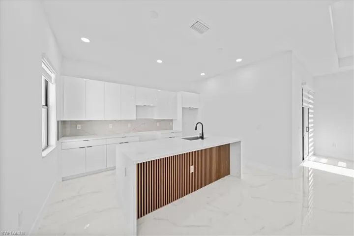 Modern kitchen featuring white cabinetry, a large center island with a wood-slat accent panel, quartz countertops, a black gooseneck faucet, and white tile flooring