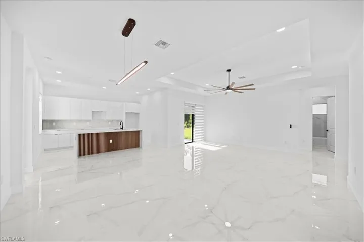 Spacious open-concept interior featuring large format marble-look tile flooring, a modern kitchen island with slatted wood paneling, white flat-panel cabinetry, and contemporary pendant lighting