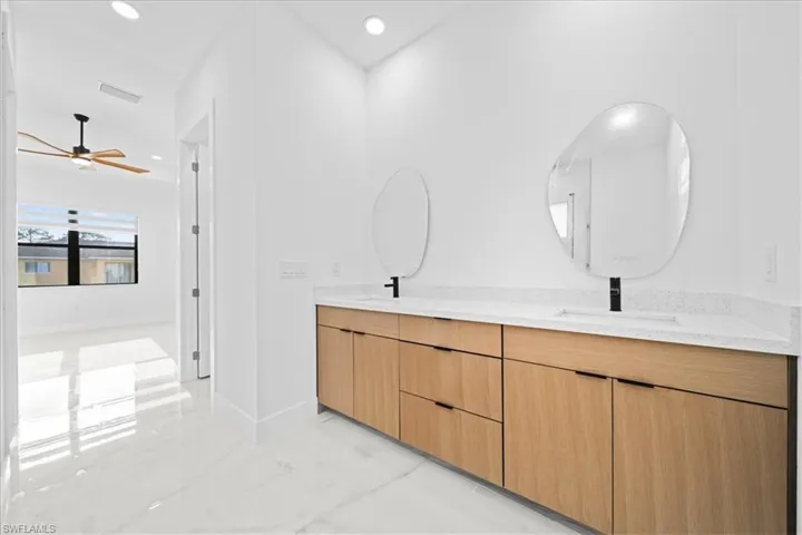 Modern bathroom vanity featuring a light wood-finish cabinetry, a white countertop with integrated sinks, and two contemporary frameless mirrors