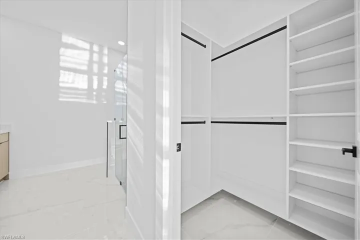 Walk-in closet featuring white built-in shelving, multiple hanging rods, and a white tile floor