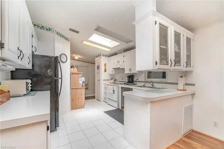 Kitchen featuring light wood-type flooring, white electric stove, a skylight, white cabinets, and kitchen peninsula