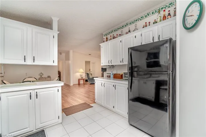 Kitchen featuring light tile patterned flooring, white cabinets, black fridge, and a textured ceiling