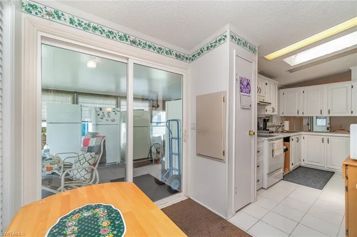 Kitchen featuring white appliances, lofted ceiling with skylight, white cabinetry, and light tile patterned floors