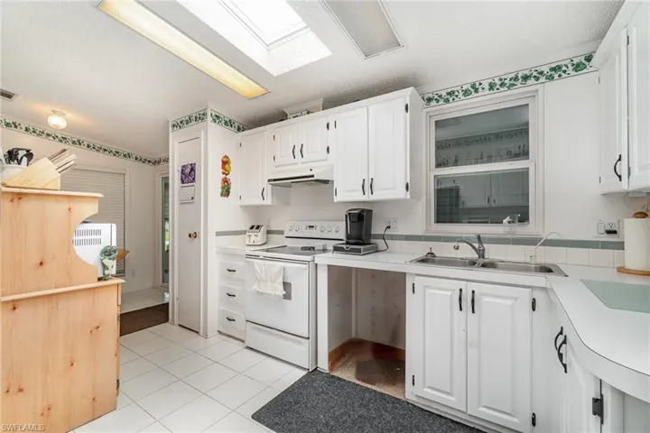 Kitchen featuring white cabinets, a skylight, light tile patterned floors, electric stove, and sink