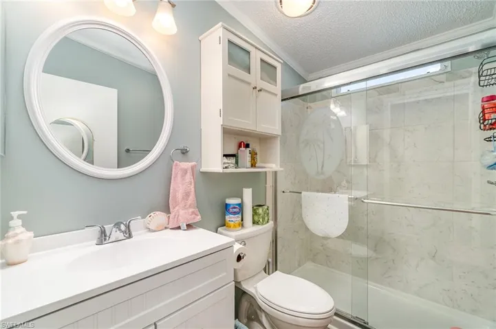 Bathroom featuring a textured ceiling, toilet, vanity, ornamental molding, and a shower with shower door