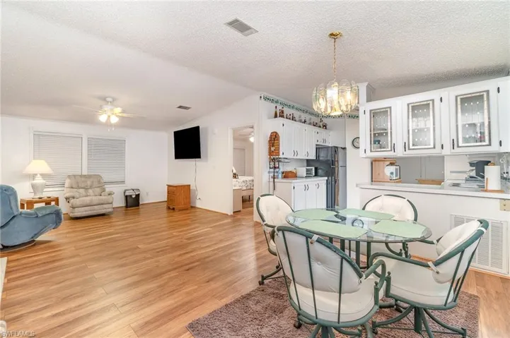 Dining area with light wood-type flooring, a textured ceiling, ceiling fan with notable chandelier, and vaulted ceiling