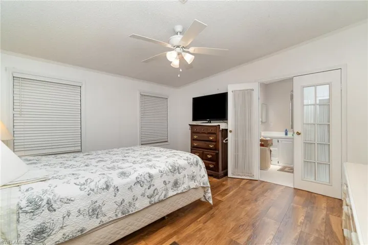 Bedroom featuring ceiling fan, hardwood / wood-style flooring, vaulted ceiling, ensuite bath, and ornamental molding