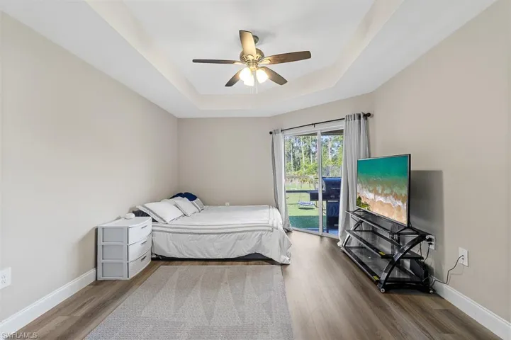 Bedroom with baseboards, access to exterior, wood finished floors, and a raised ceiling