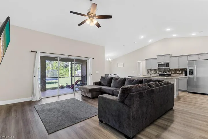 Living area featuring a ceiling fan, light wood-style flooring, high vaulted ceiling, and baseboards
