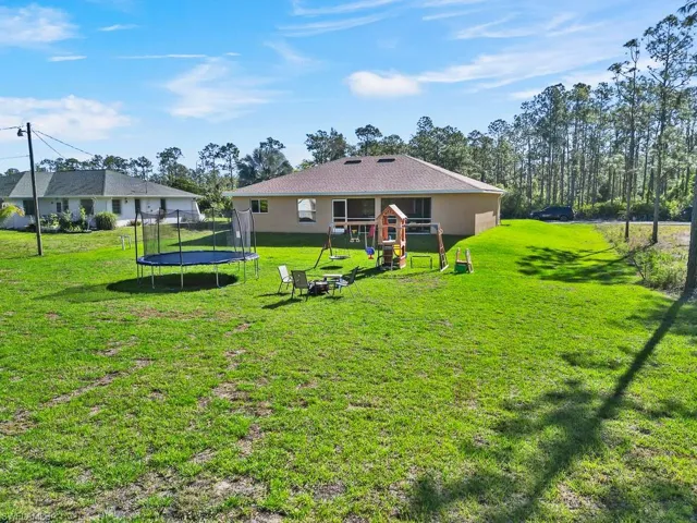 Back of house with a playground, a lawn, stucco siding, and a trampoline