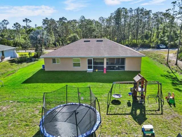 Back of property with a playground, a yard, stucco siding, and a trampoline