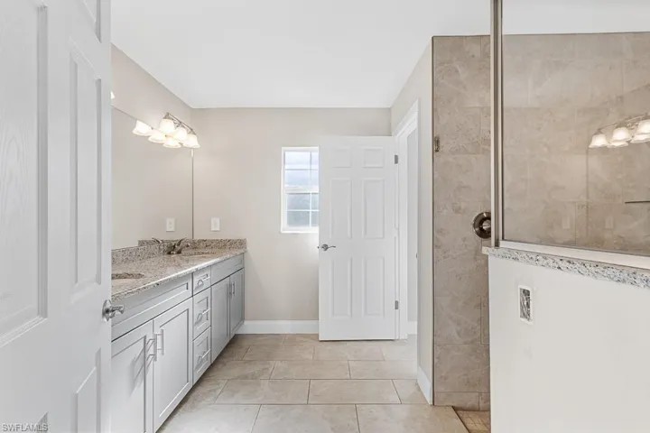 Bathroom with tile patterned flooring, baseboards, a sink, walk in shower, and double vanity