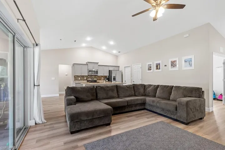 Living area featuring a ceiling fan, high vaulted ceiling, baseboards, and light wood finished floors