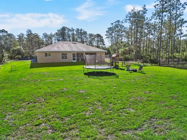 Back of house with a lawn, a trampoline, a playground, and stucco siding