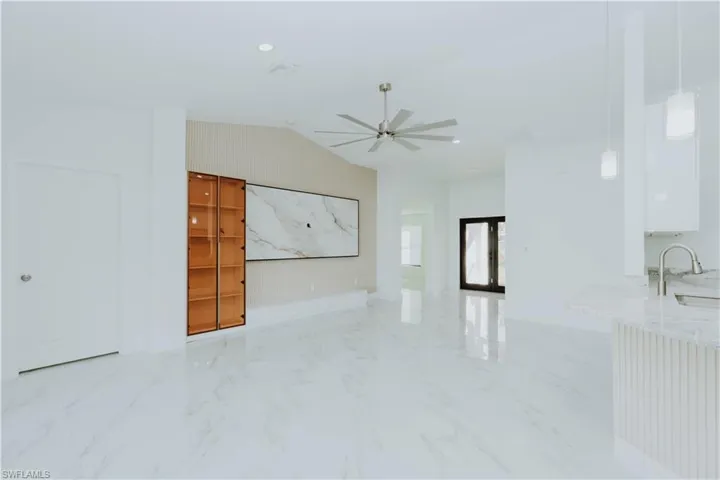 Kitchen featuring appliances with stainless steel finishes, light marble finish floors, white cabinets, lofted ceiling, and light stone counters