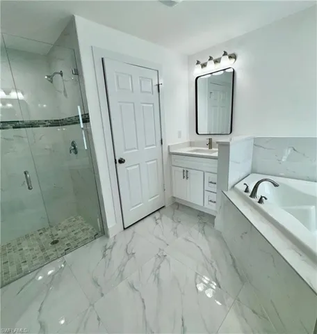 Full bathroom with vanity, a marble finish shower, a garden tub, and light marble finish flooring
